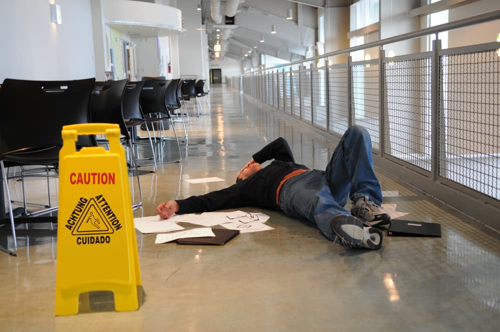 Man lies on the wet floor on which he slipped in spite of caution sign, selective focus on man's head