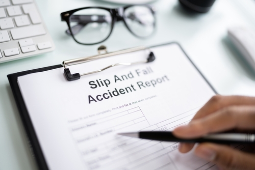 Close-up of a person filling out a “Slip and Fall Accident Report” form on a clipboard beside eyeglasses and a keyboard.