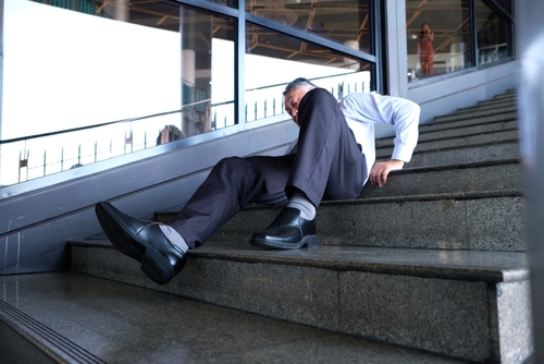 Middle-aged man in business attire lying on a staircase after a fall, appearing injured and in pain.