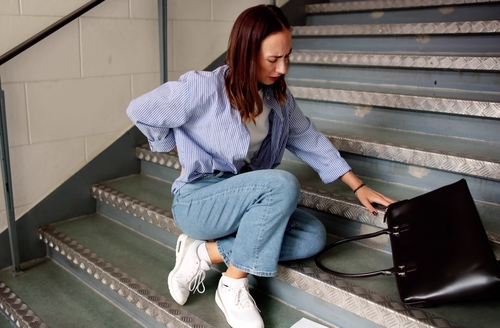 Injured woman sitting on stairs holding her back.